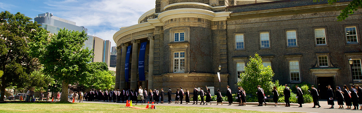 Landscape image of U of T students in graduation gowns outside of Convocation Hall.
