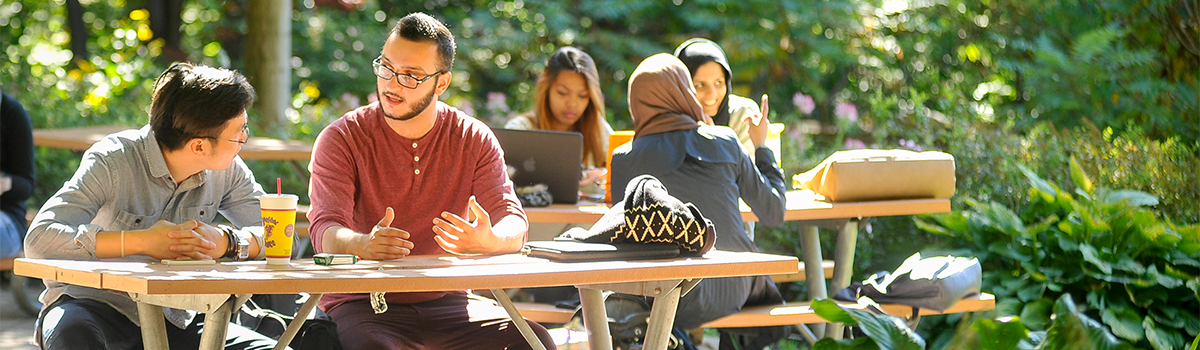 Students sitting on picnic tables outdoors talking and interacting.