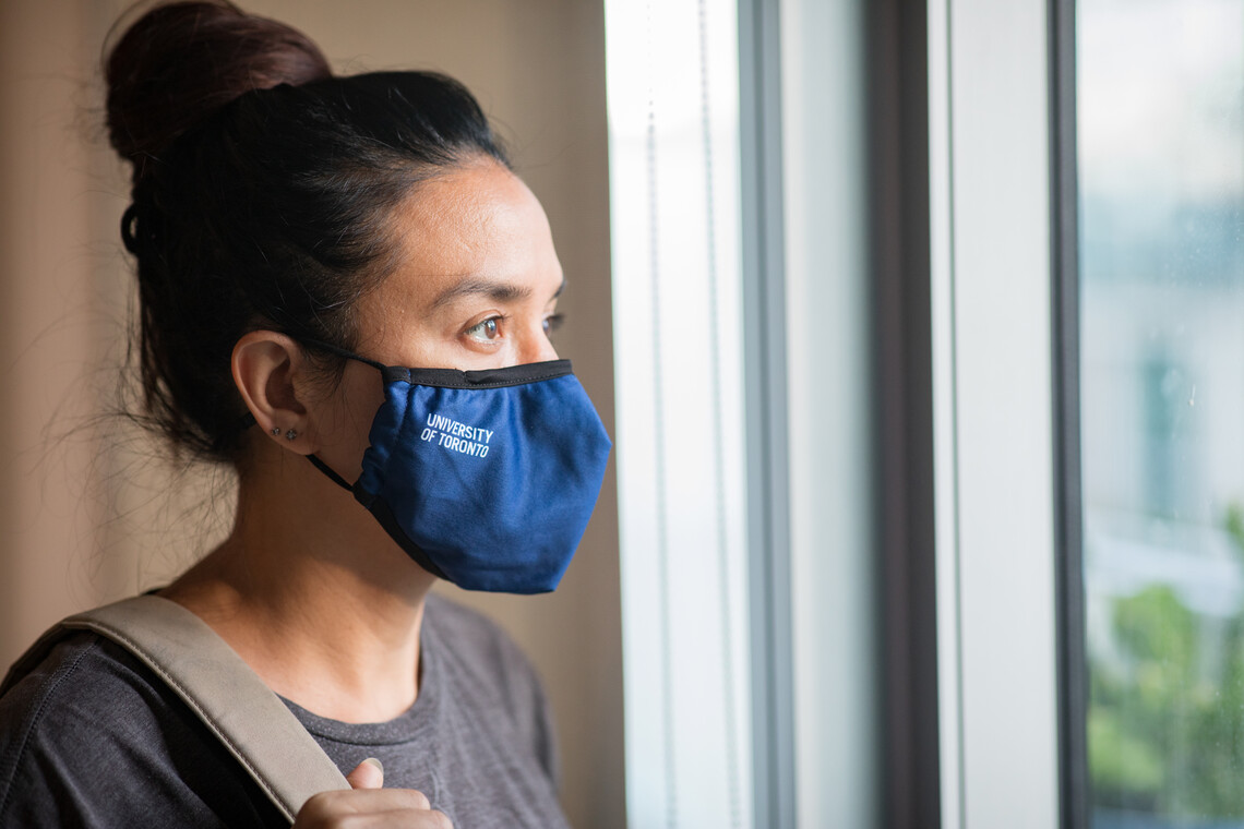 Person wearing U of T branded face mask and looking out a window.