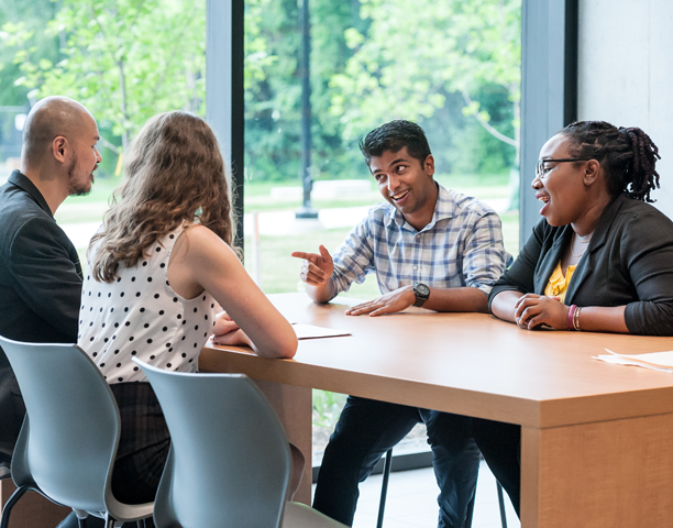 Four U of T staff members sitting in a meeting room at a table talking.