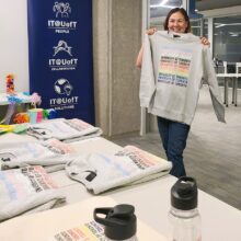 Carrie Schmidt, Senior Manager, showcasing U of T Pride swag at the in-office Pride coffee break celebration.