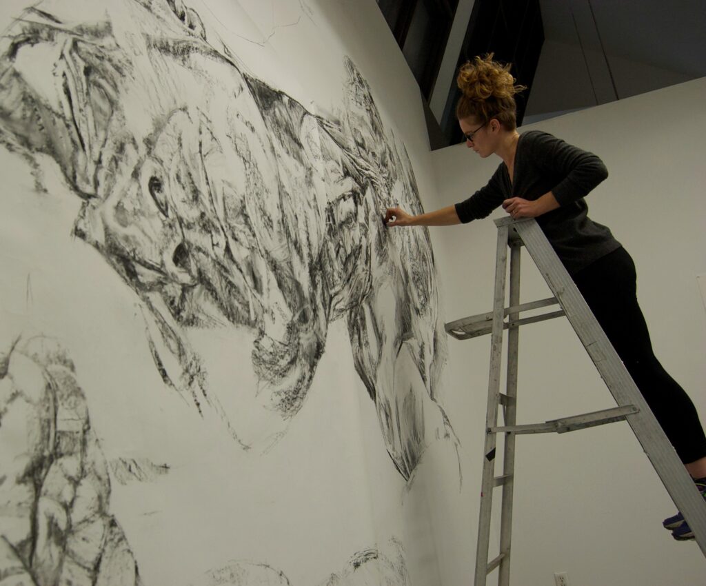 Esther standing on a ladder, drawing with vine charcoal on a wall