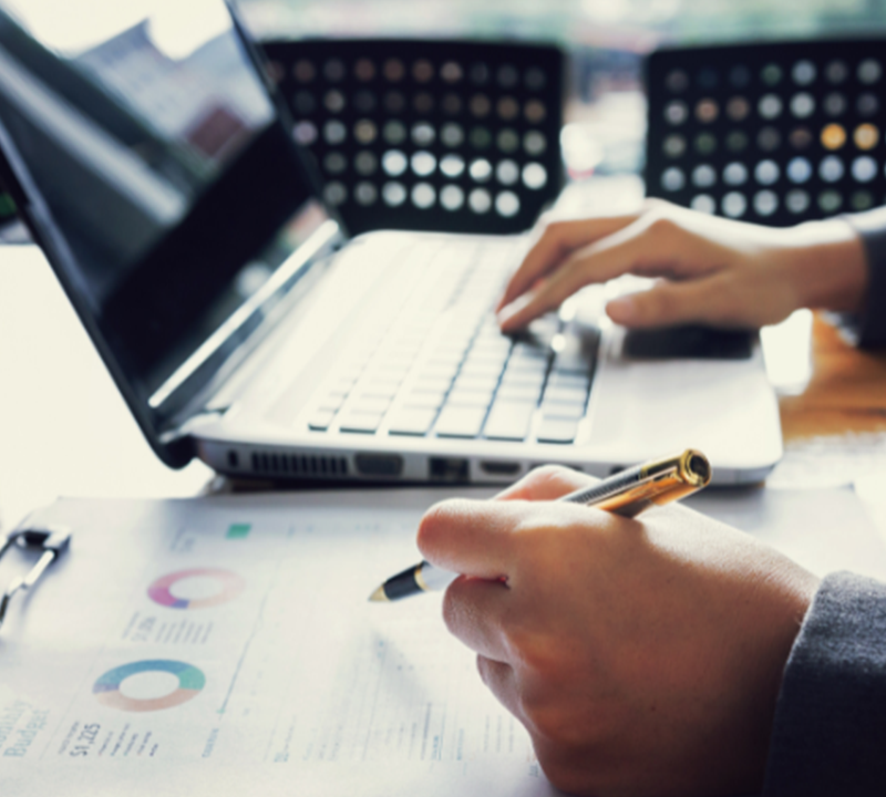 A person working on a laptop while cross-referencing a report