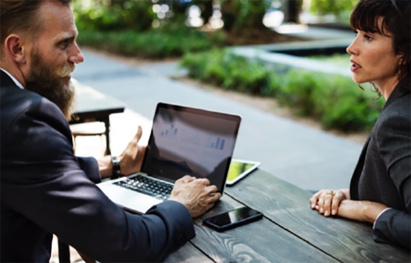 Two people having a conversation while using a laptop